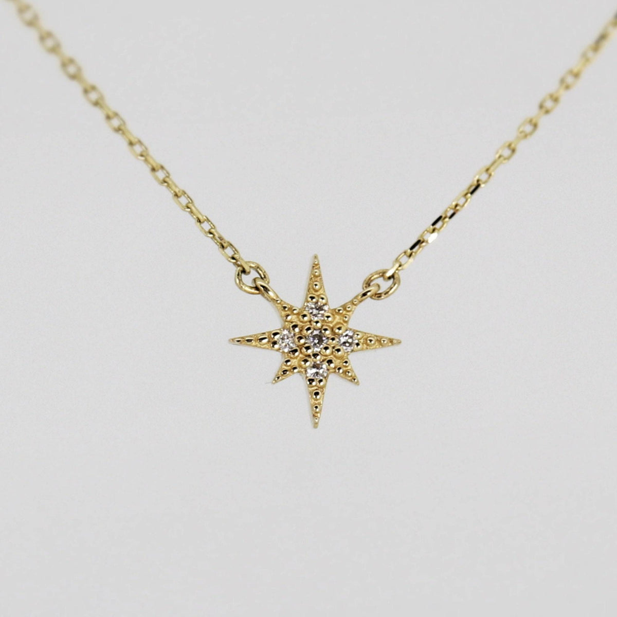 A gold chain necklace with a small, flat, eight-point star pendant, encrusted with tiny clear stones, against a plain white background.