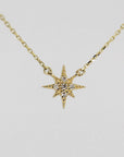 A gold chain necklace with a small, flat, eight-point star pendant, encrusted with tiny clear stones, against a plain white background.