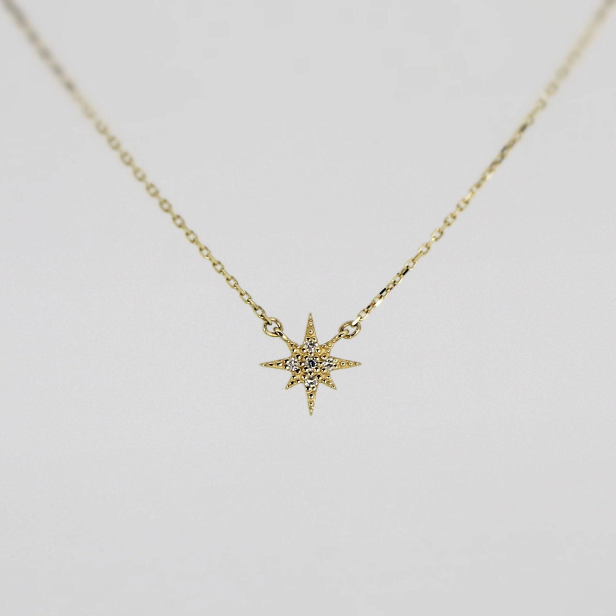A gold chain necklace with a small, flat, eight-point star pendant, encrusted with tiny clear stones, against a plain white background.