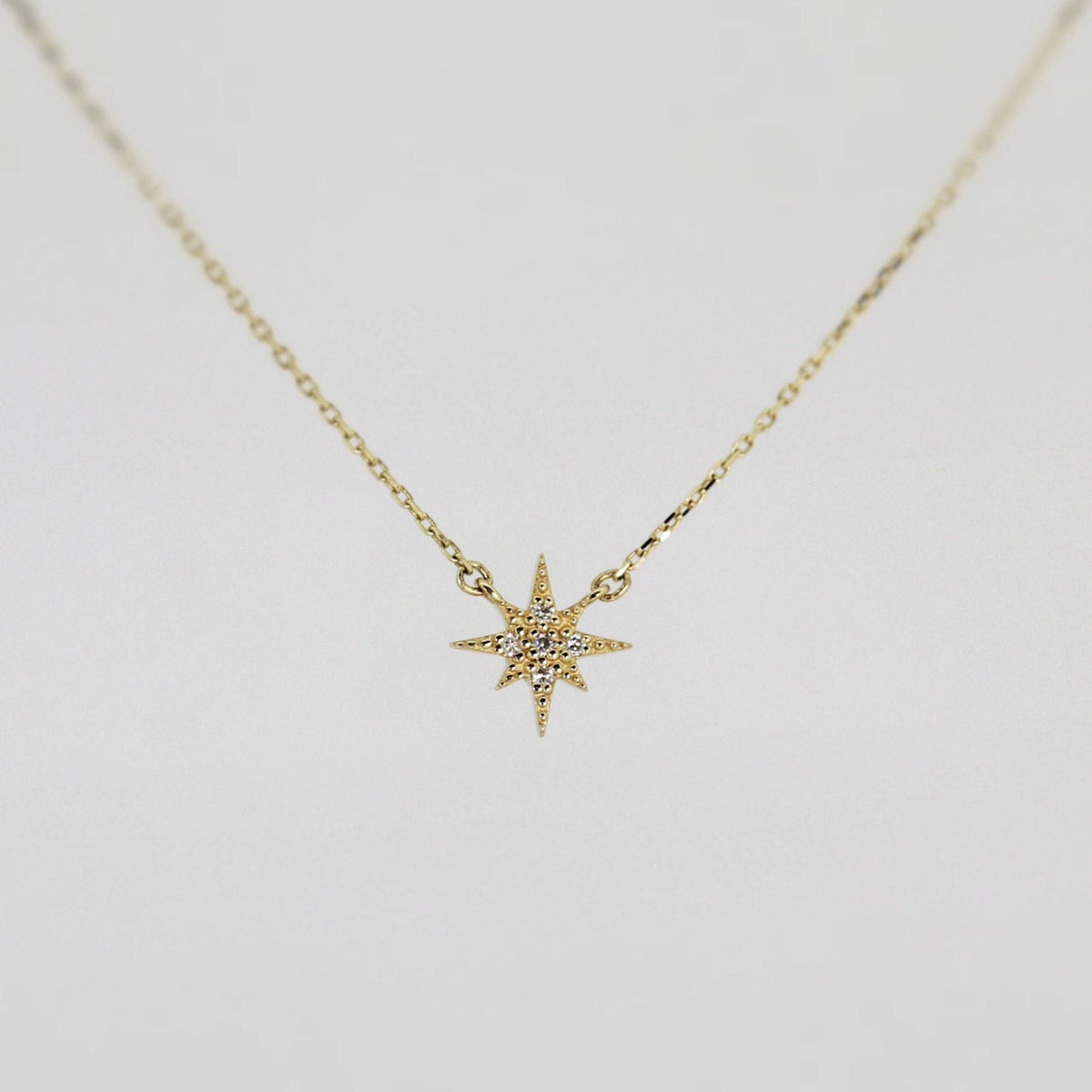 A gold chain necklace with a small, flat, eight-point star pendant, encrusted with tiny clear stones, against a plain white background.