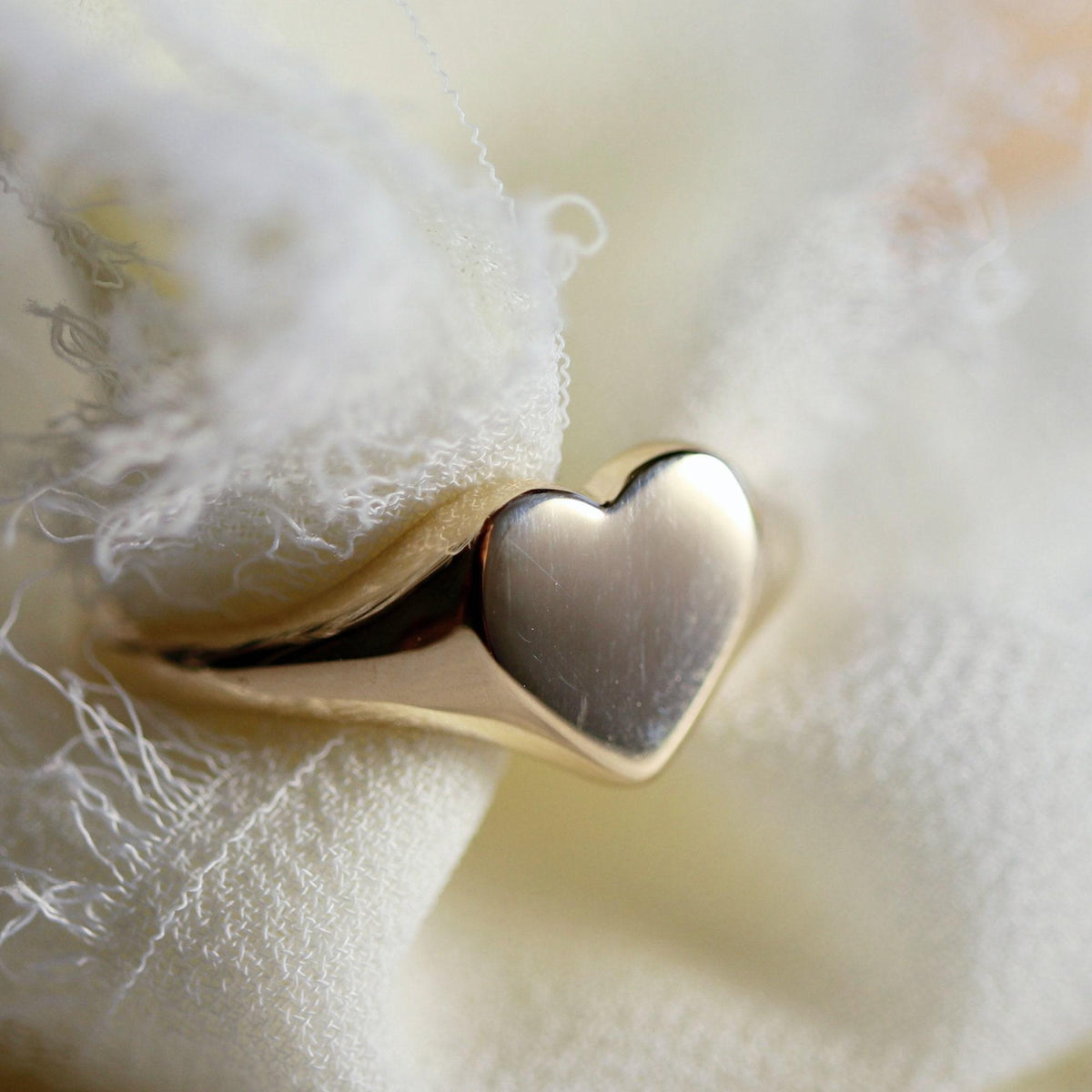 A gold heart-shaped signet ring resting on a textured, light-colored fabric.