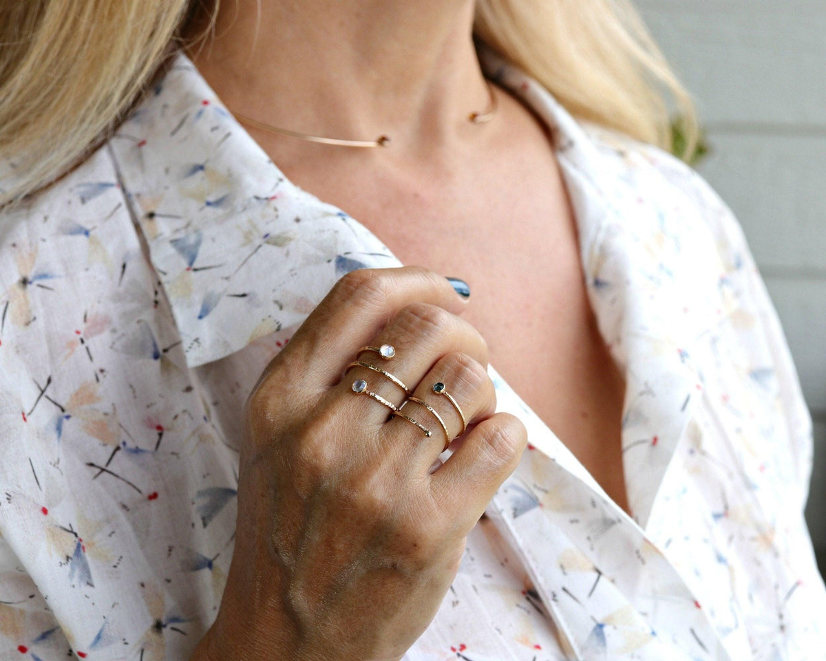 A person wearing a textured gold spiral ring on their finger and a matching thin choker necklace.