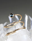 A textured gold wrap ring with a dark blue stone on one end resting on a cluster of raw quartz crystals.