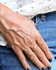 A hand wearing several thin gold rings rests against blue denim shorts.