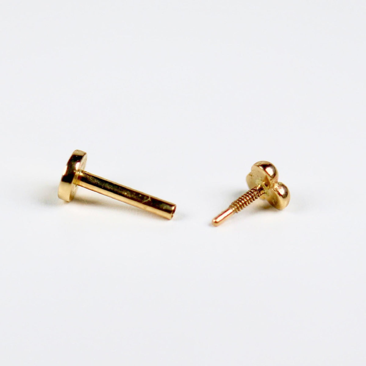 Disassembled gold flat back labret stud showing the threaded post and trinity ball top separated on a white surface.