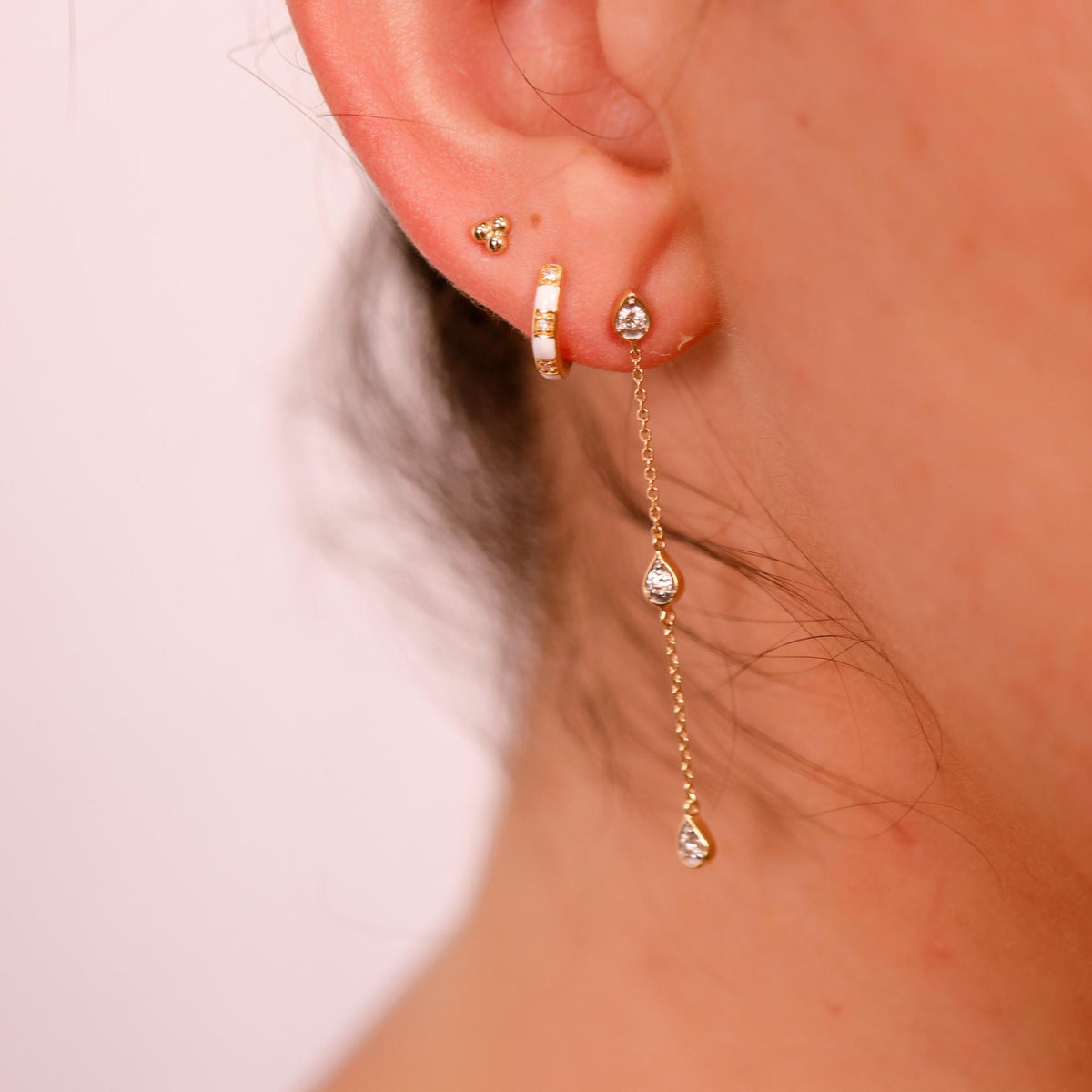 Close-up of a human ear wearing a tiny gold trinity stud in the uppermost cartilage piercing.
