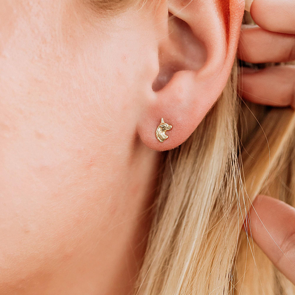 Close up of a person's earlobe wearing a small gold unicorn head stud earring.