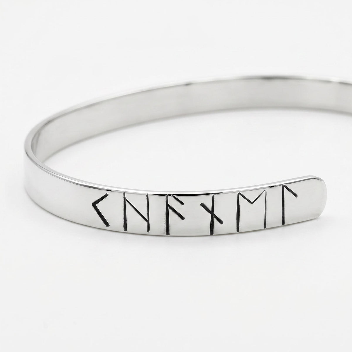 An angled close-up view of a polished silver-colored metal cuff bracelet displaying a sequence of stamped rune symbols.