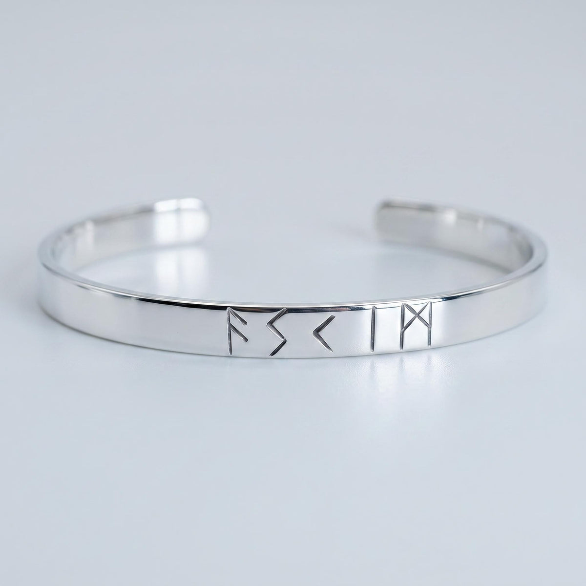 A front view of a polished silver-colored open metal cuff bracelet displaying stamped rune symbols against a neutral light background.