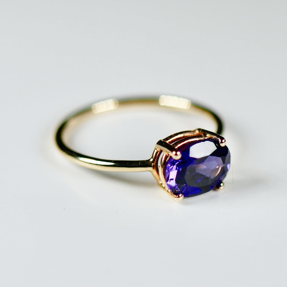 Side-angle view of a gold ring showcasing the basket setting and prong details holding an oval purple gemstone.
