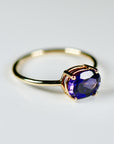 Side-angle view of a gold ring showcasing the basket setting and prong details holding an oval purple gemstone.