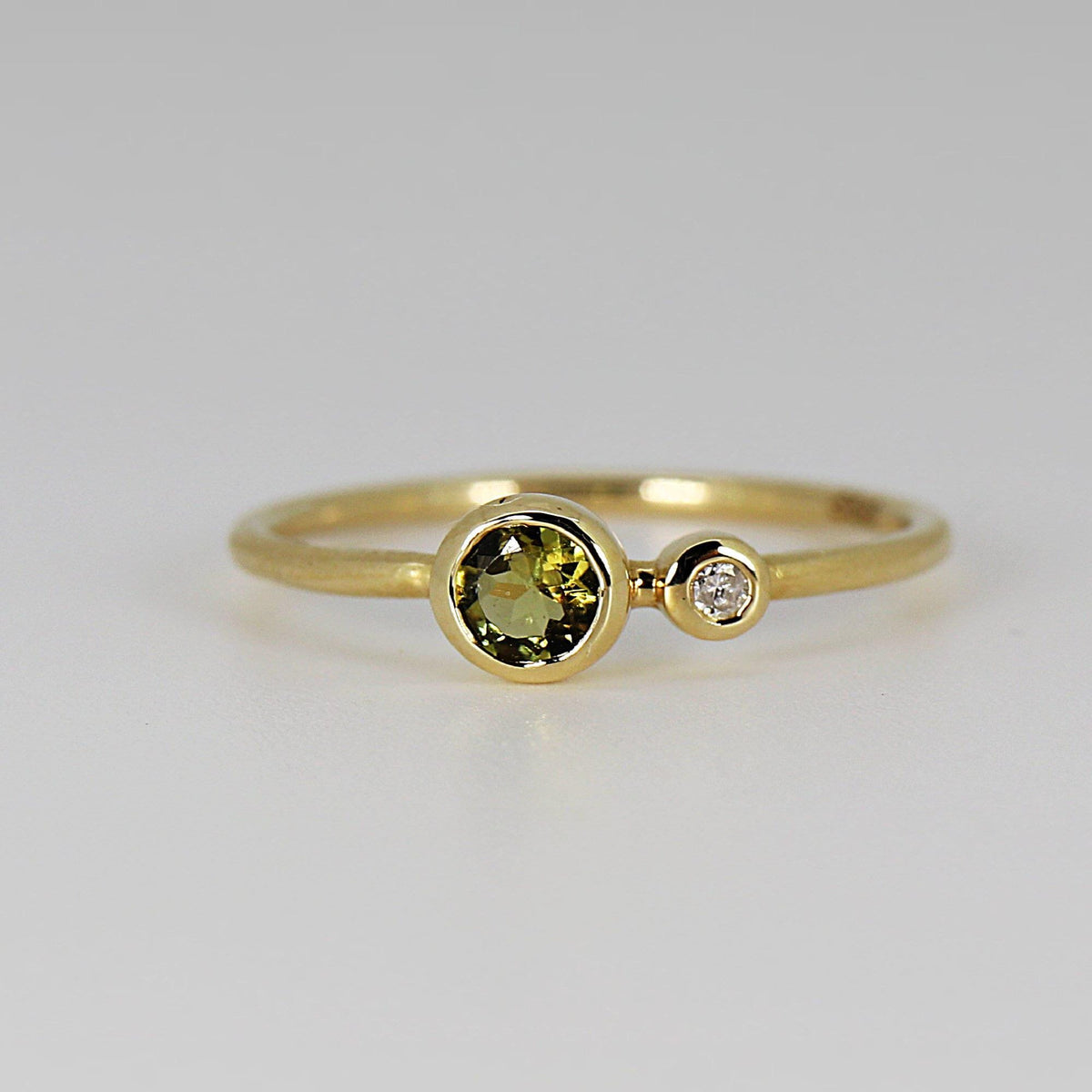 Front view of the yellow gold dual birthstone ring showcasing the large round green tourmaline next to the smaller round diamond in bezel settings.