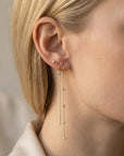 Close-up side profile of a blond woman wearing a stud earring and long gold threader earrings with bezel-set diamonds.