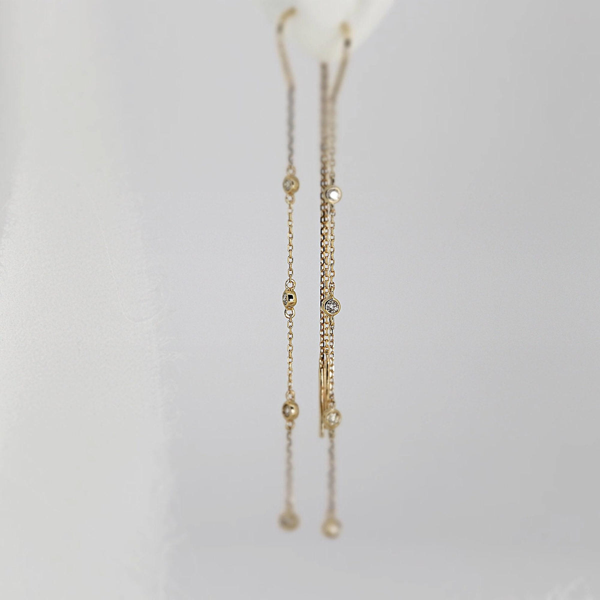 A close-up of gold threader earrings with embedded small diamonds hanging against a soft white background.