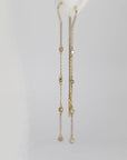 A close-up of gold threader earrings with embedded small diamonds hanging against a soft white background.