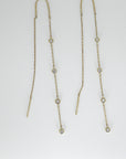 Two gold threader earrings with bezel-set diamond stations laid flat on a plain white surface.