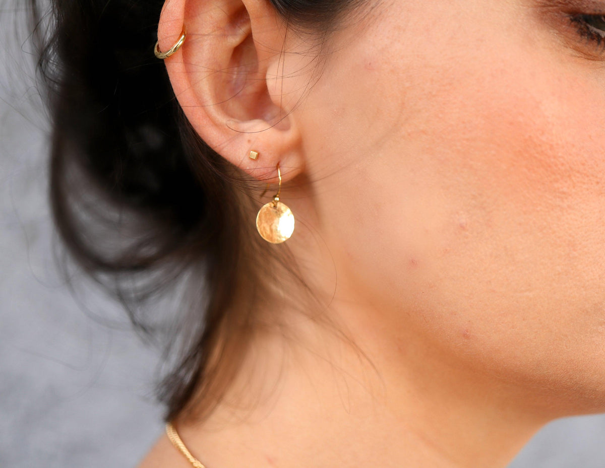 Side view of a person wearing a small gold hammered disc earring and ear cuffs.