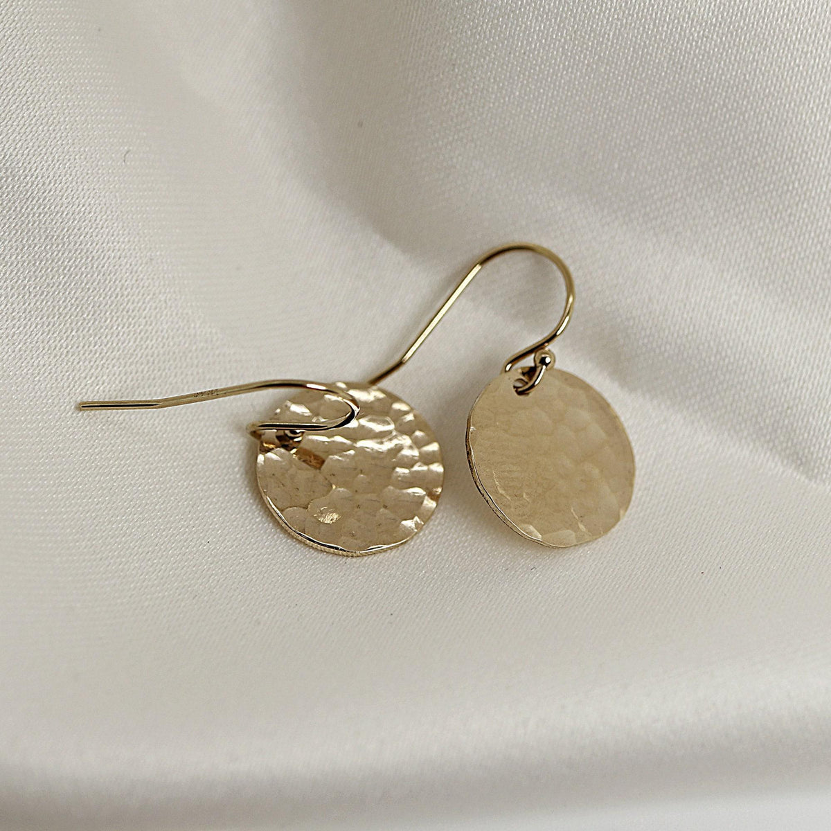 Gold hook earrings with round textured drops displayed on white silk.