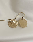 Gold hook earrings with round textured drops displayed on white silk.