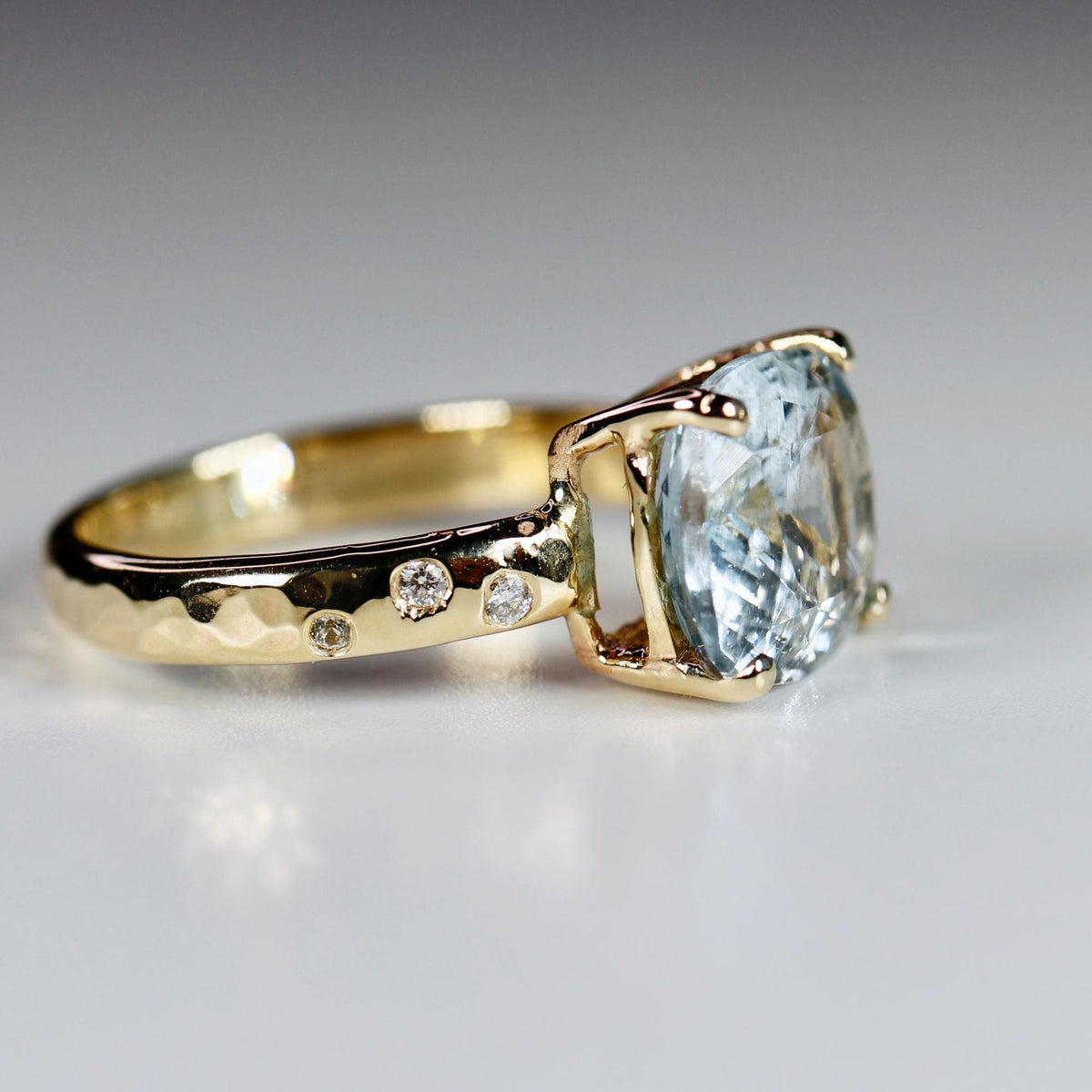 The opposite side profile of the gold ring on a white surface, showing the hammered band texture and small flush-set accent diamonds.