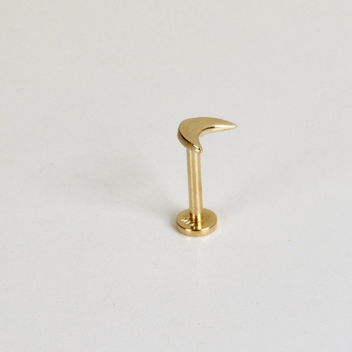 A gold crescent moon flat back stud earring standing upright on a white surface.