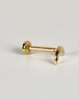 A gold flat back labret stud with a crescent moon top lying horizontally on a plain white surface.