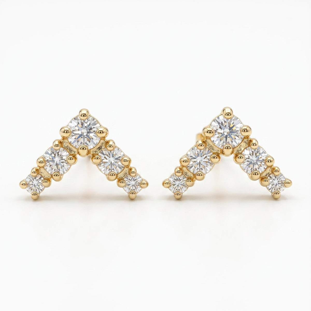 Two gold chevron stud earrings set with small round diamonds lie flat against a white background.