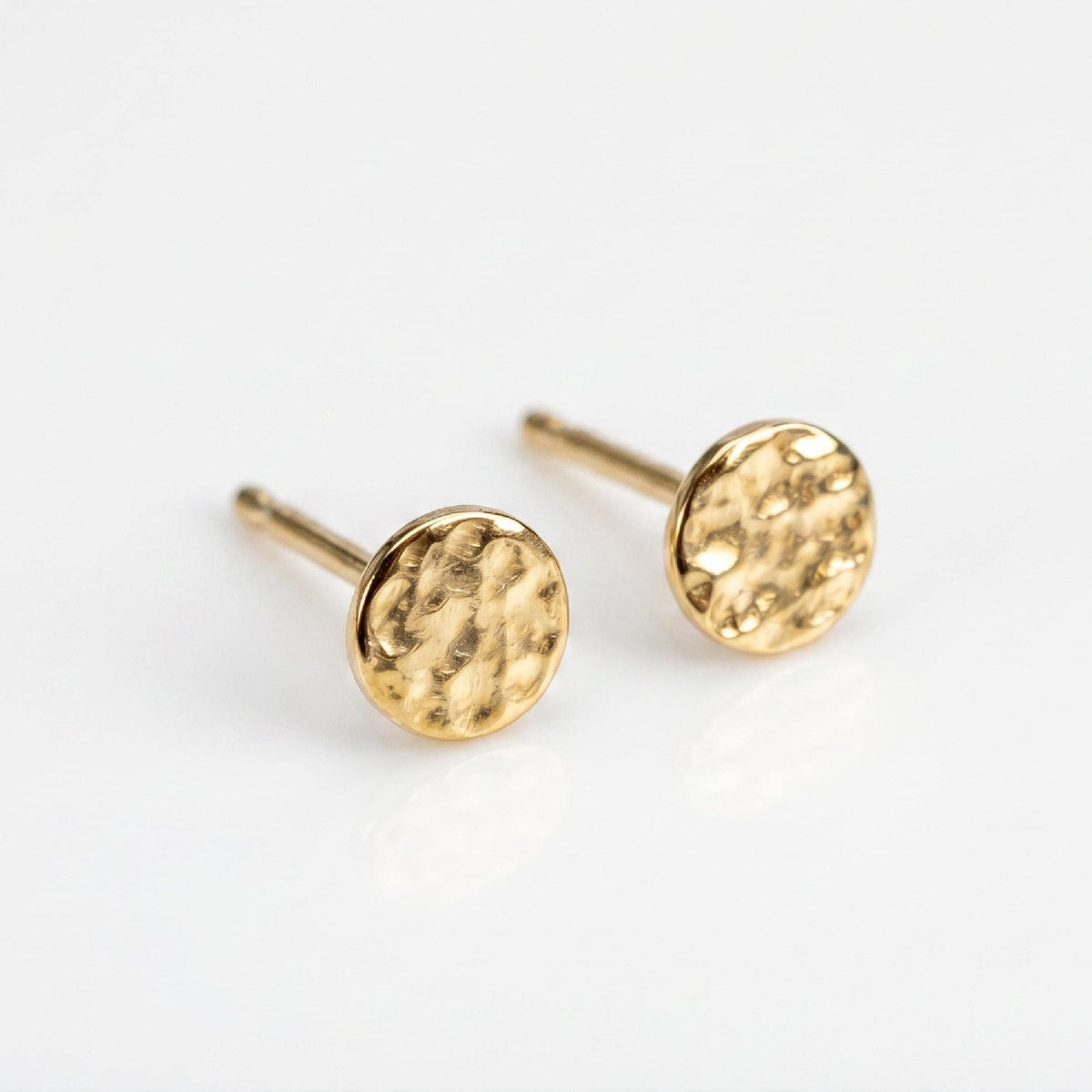 Two small round gold stud earrings with a hammered texture rest on a white surface.