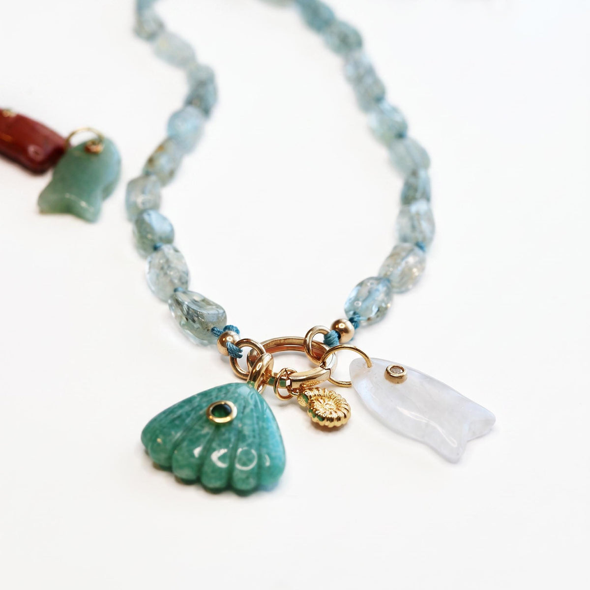 An aquamarine nugget necklace with a gold charm holder ring attached, featuring a green shell charm and a white fish charm.