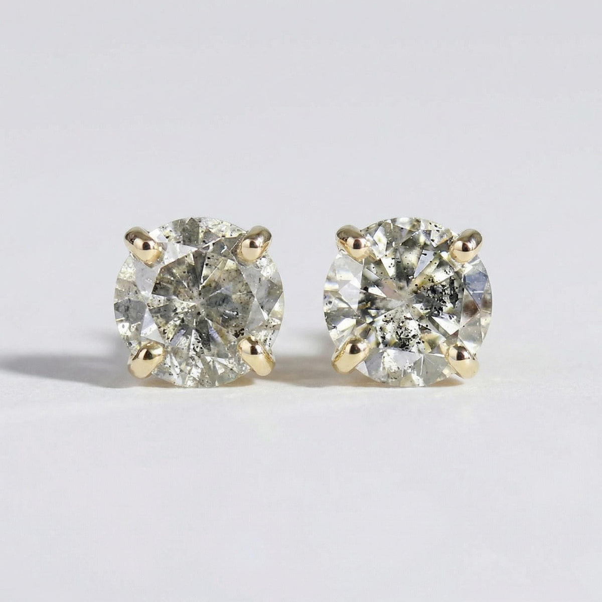 Two round salt and pepper diamond stud earrings set in four-prong yellow gold settings on a white background.