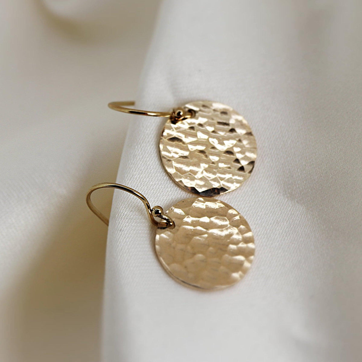 Two round gold disc earrings rest against white fabric.