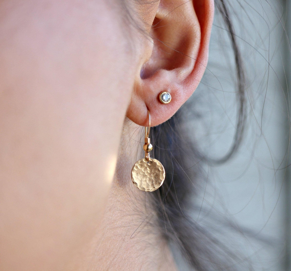 Close-up shot of a single gold hammered disc drop earring worn on an ear lobe.