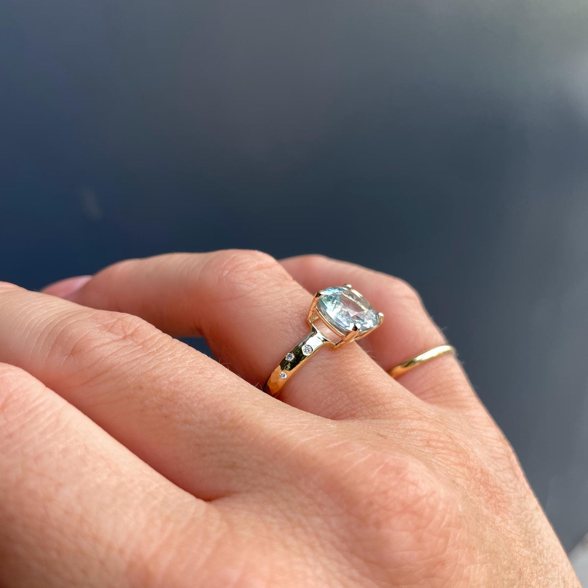 A close-up view of a hand wearing the gold ring with a large light blue gemstone and small accent stones.