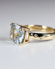 A close-up side angle of the gold ring showcasing the prong-set light blue cushion-cut main stone and three flush-set accent diamonds.