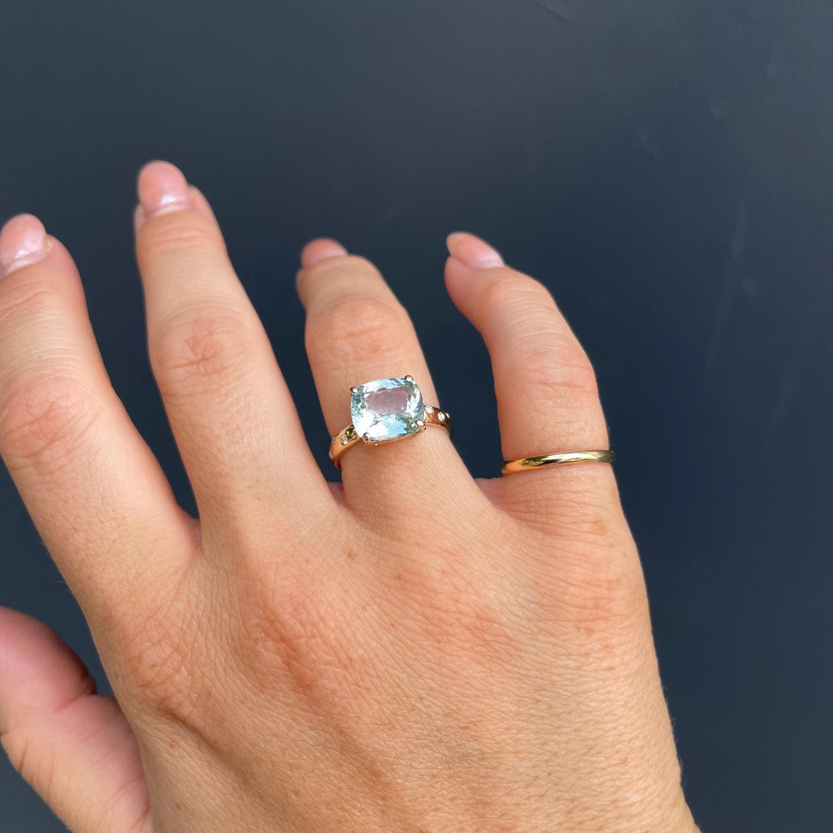 A straight-on view of the hand wearing the gold ring with the large light blue gemstone on the ring finger.