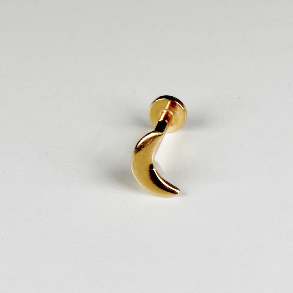 A gold crescent moon flat back labret stud earring angled on a light surface.