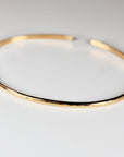 A single hammered gold open cuff bracelet rests flat on a plain white surface.