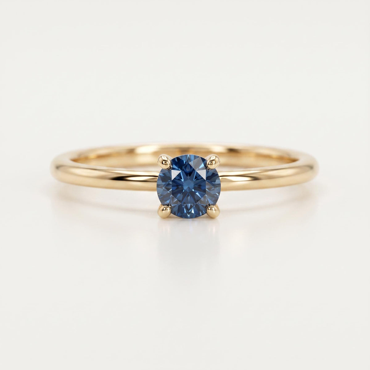 Front view of a gold ring with a round blue gemstone in a four-prong setting against a white background.