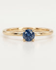 Front view of a gold ring with a round blue gemstone in a four-prong setting against a white background.