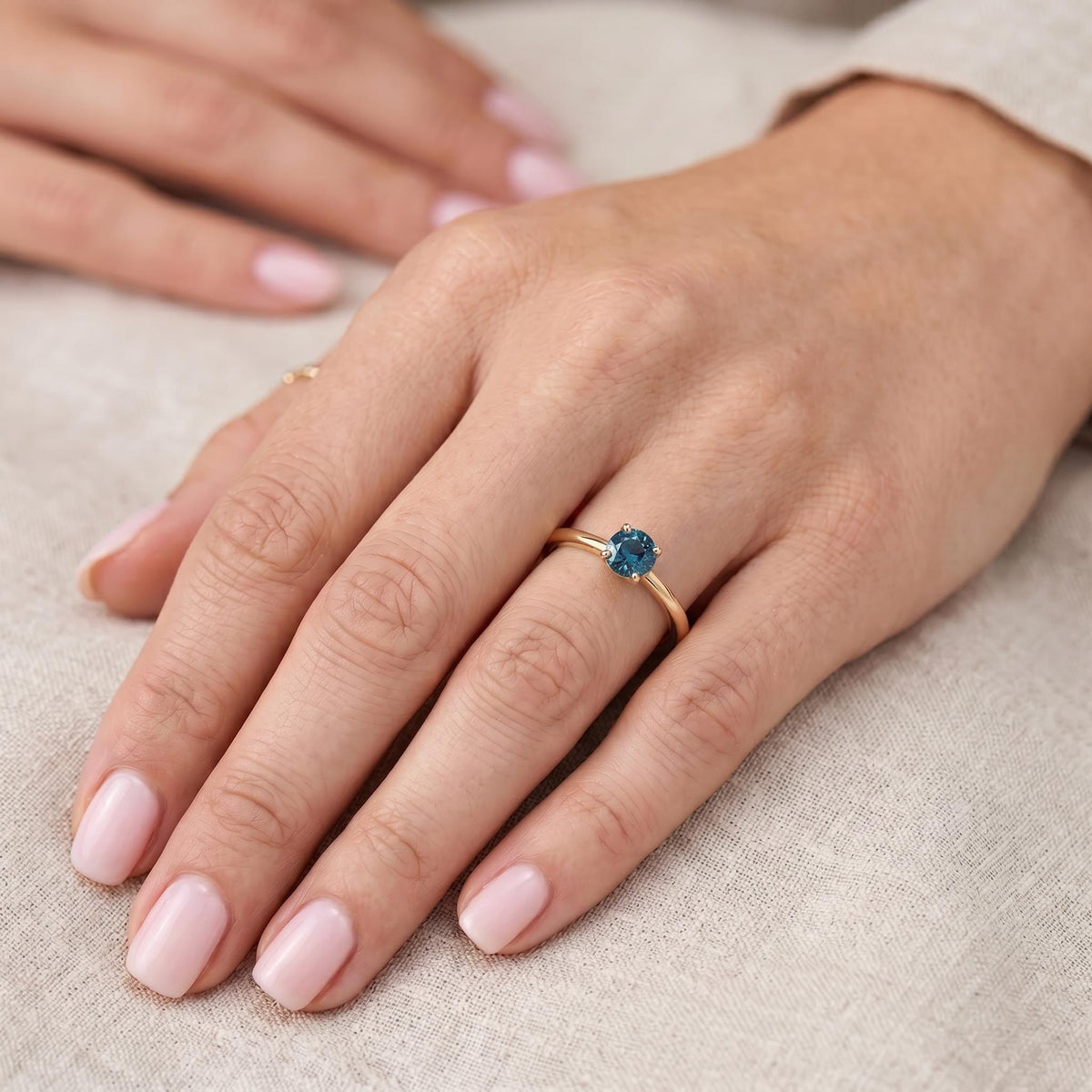 Close-up of a person wearing the delicate gold ring with a blue gemstone on their ring finger.
