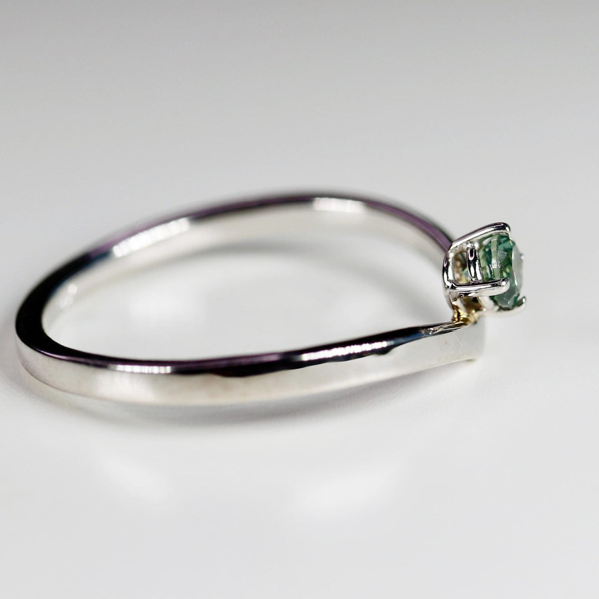 A silver-colored v-shaped wishbone ring with a small round teal gemstone prong-set at the center point.