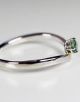 A silver-colored v-shaped wishbone ring with a small round teal gemstone prong-set at the center point.