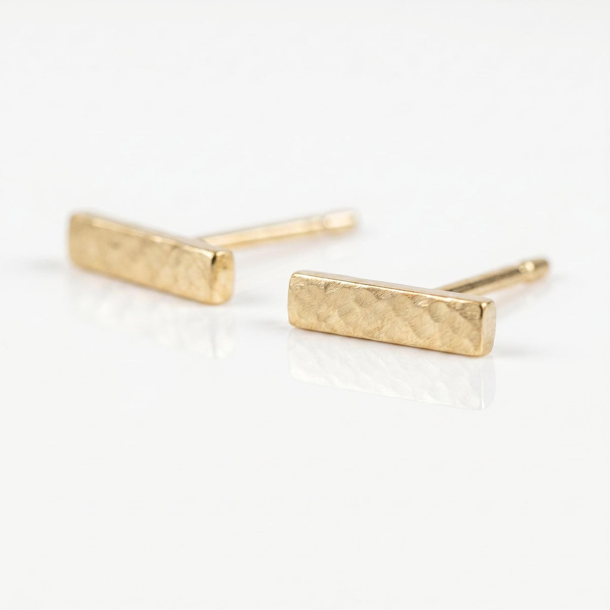 Two hammered gold bar stud earrings displayed at an angle against a white background.