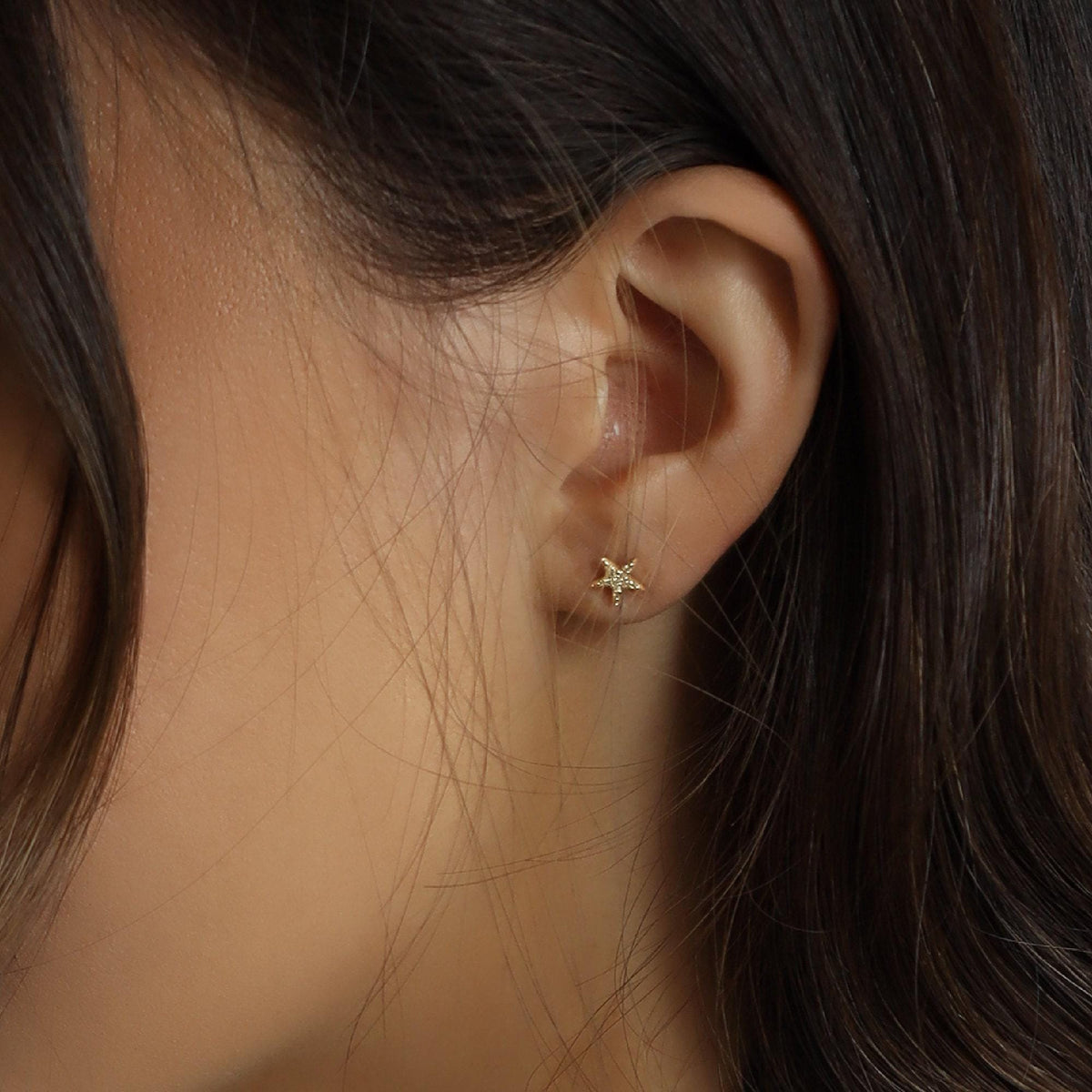 Close-up view of a person wearing a small star-shaped stud earring in the earlobe.