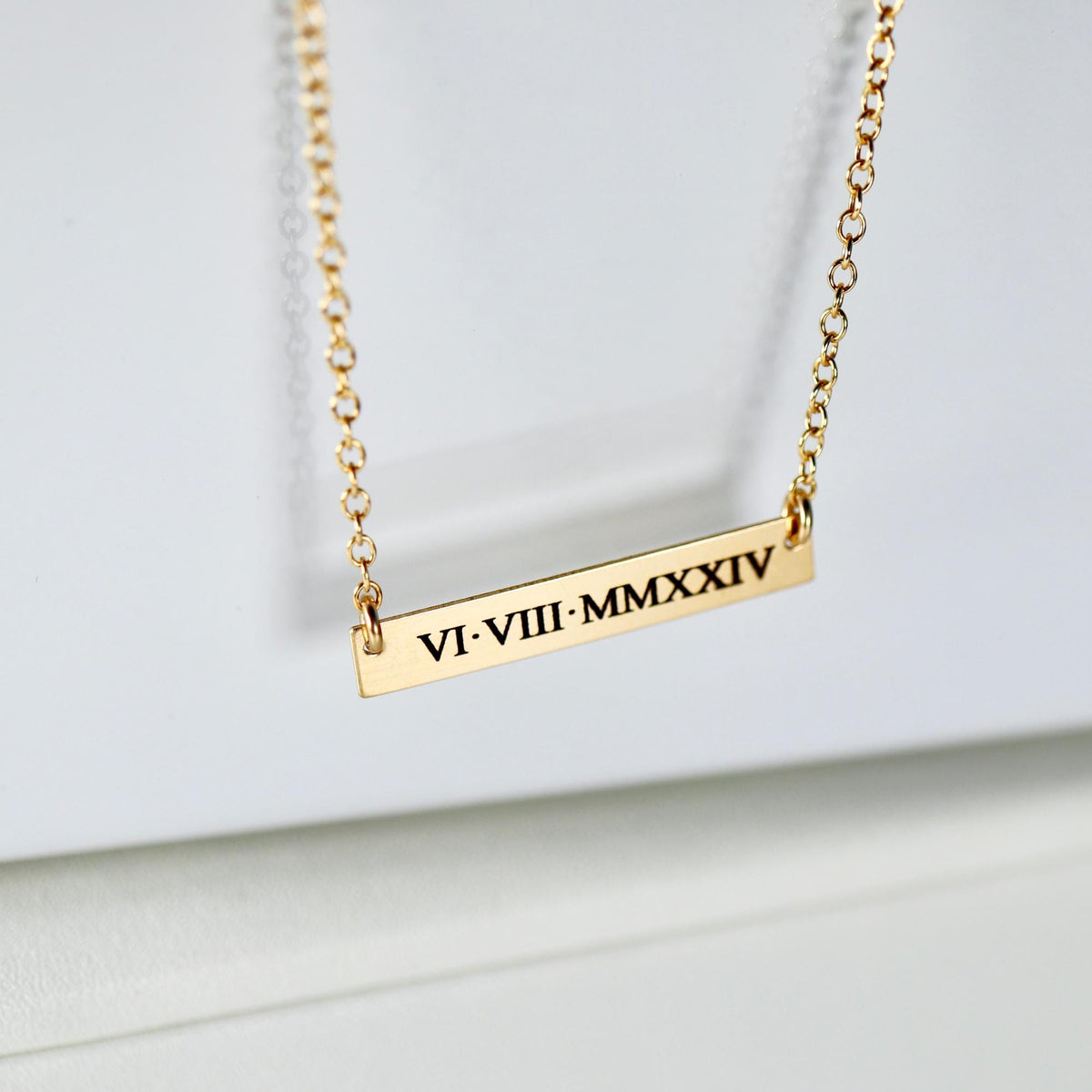 Macro view of a gold chain necklace with a rectangular bar pendant displaying roman numerals VI-VIII-MMXXIV.