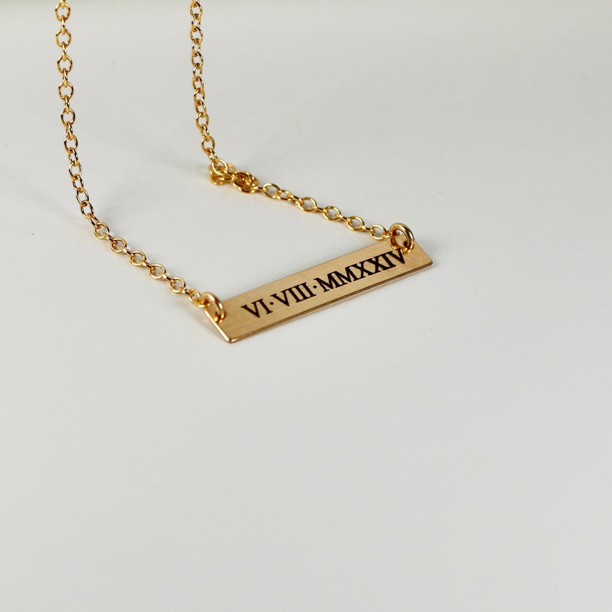 Gold necklace featuring an engraved bar pendant resting on a light surface.