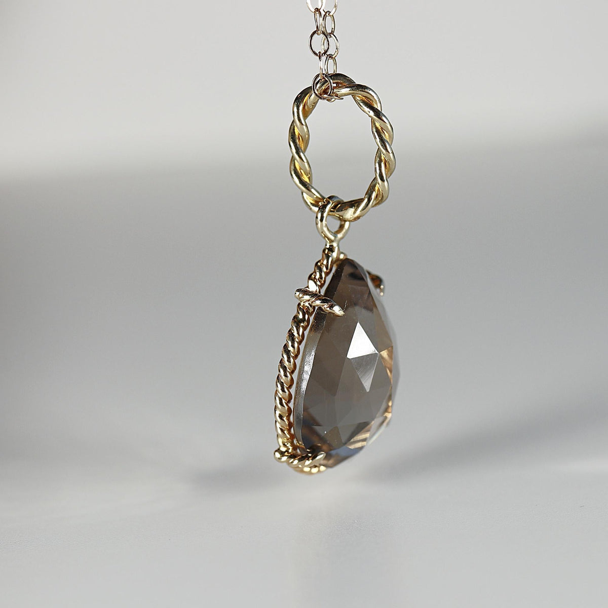 Profile view of a pear-shaped faceted smokey quartz pendant featuring a textured rope-style gold bale and trim.