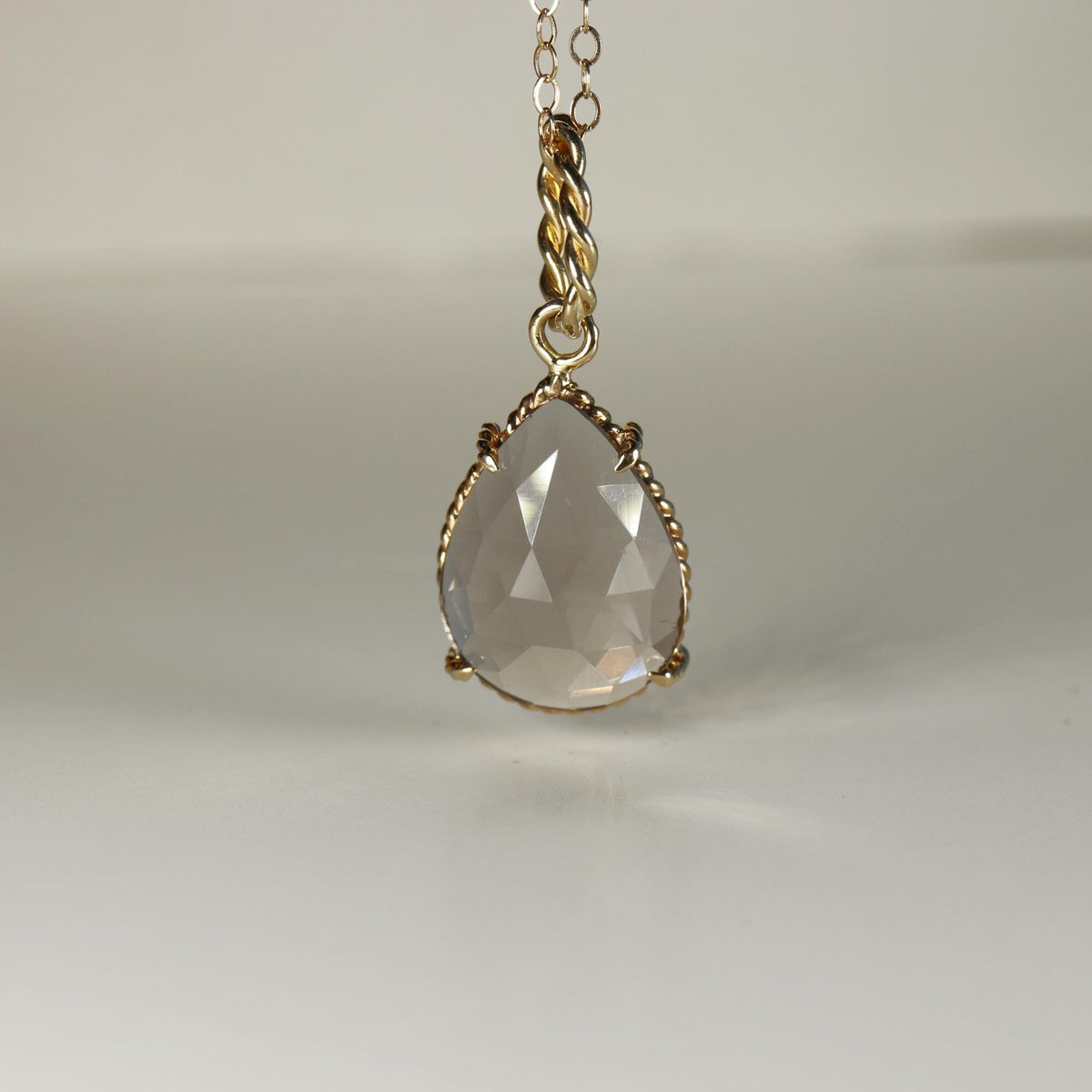 Front view of a faceted pear-shaped smokey quartz gemstone set in twisted gold against a plain surface.