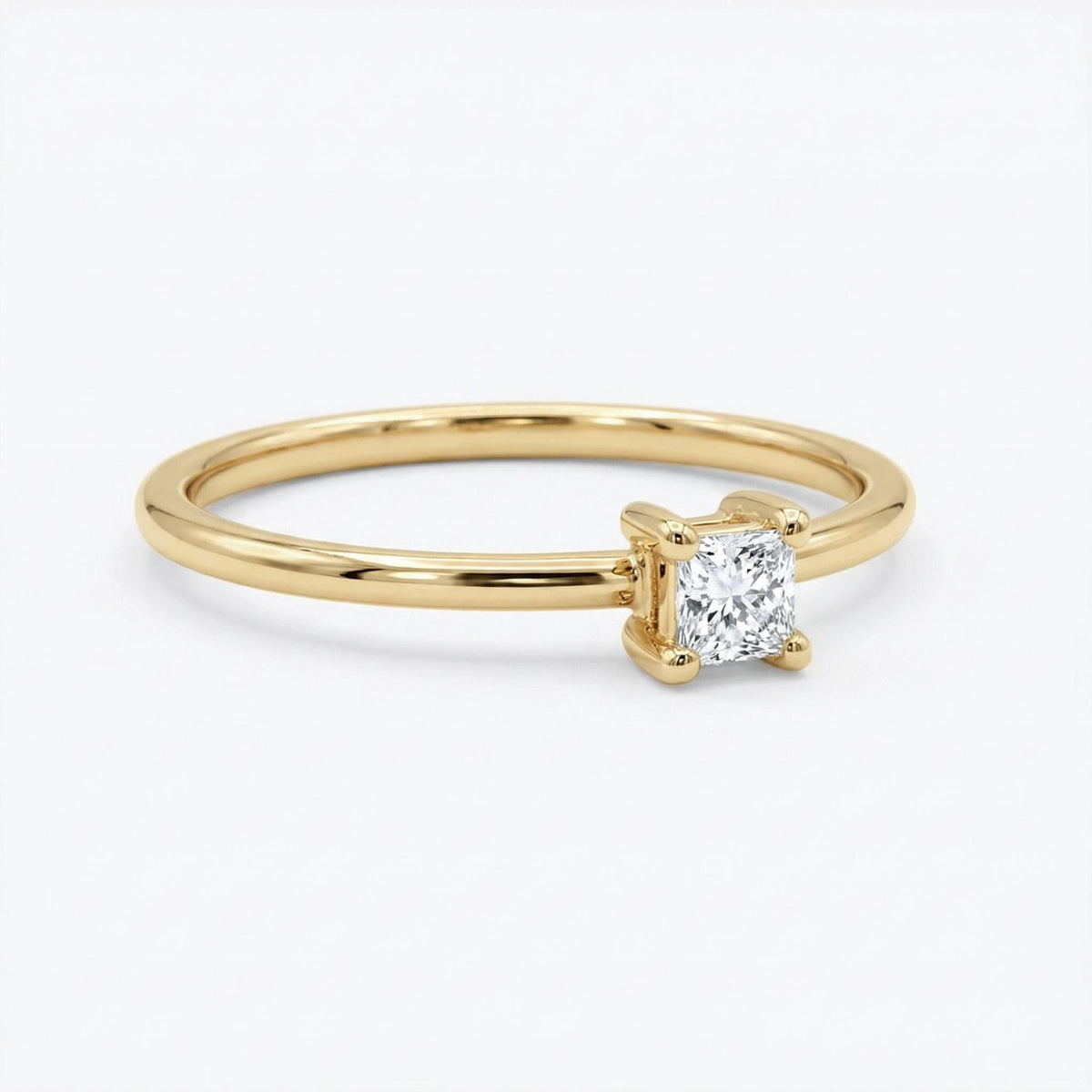 An angled view of the thin gold band with a square-cut stone in a four-prong setting on a white background.