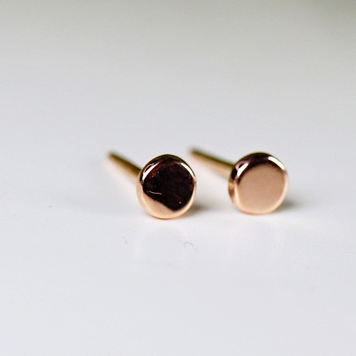 Two small rose gold dot stud earrings resting on a white surface.